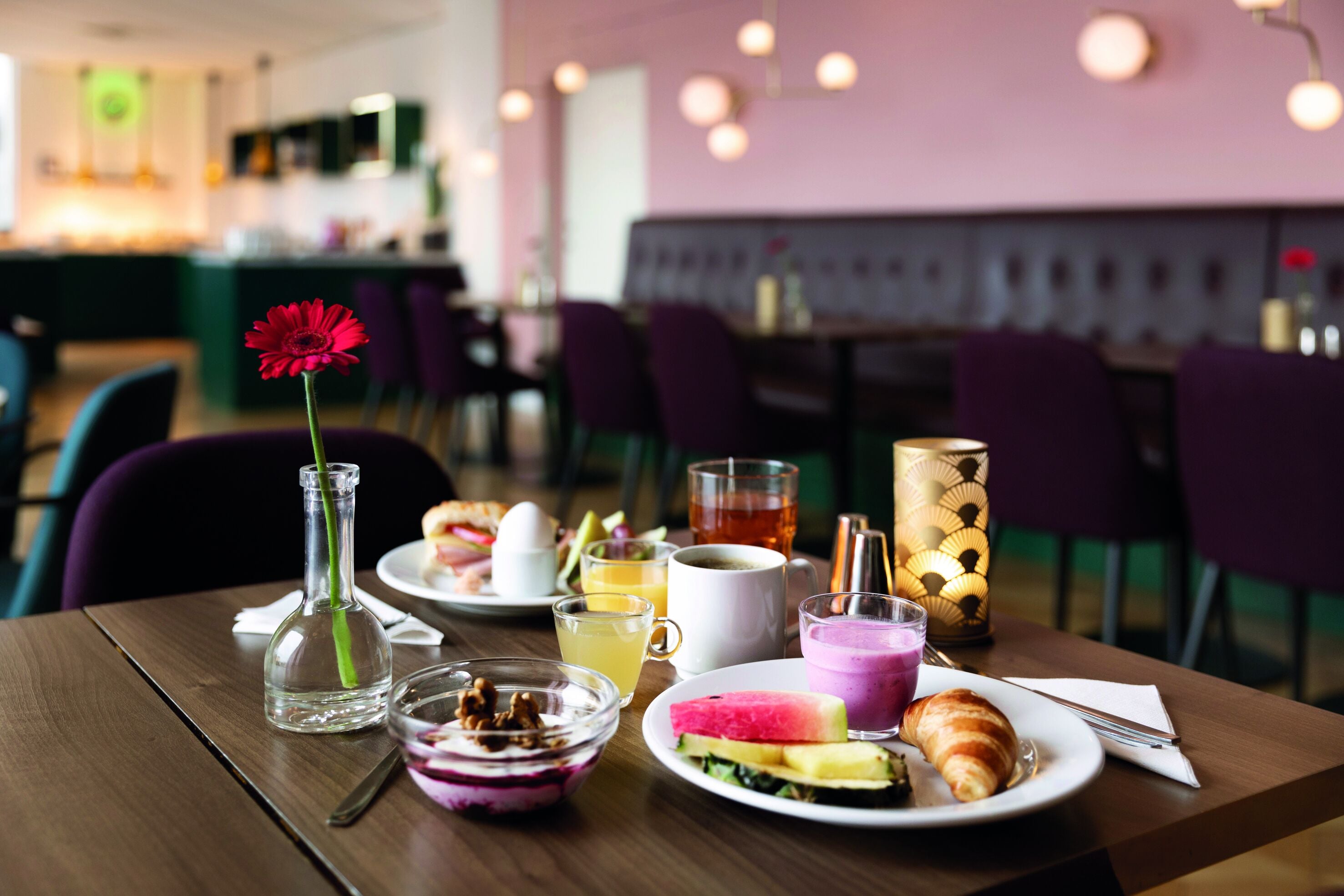 A dining table with breakfast items, including a croissant, a glass of juice, and a plate with a sandwich.