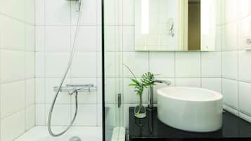 Un baño moderno con azulejos blancos, cabina de ducha de vidrio, lavamanos blanco y espejo sobre el lavamanos.