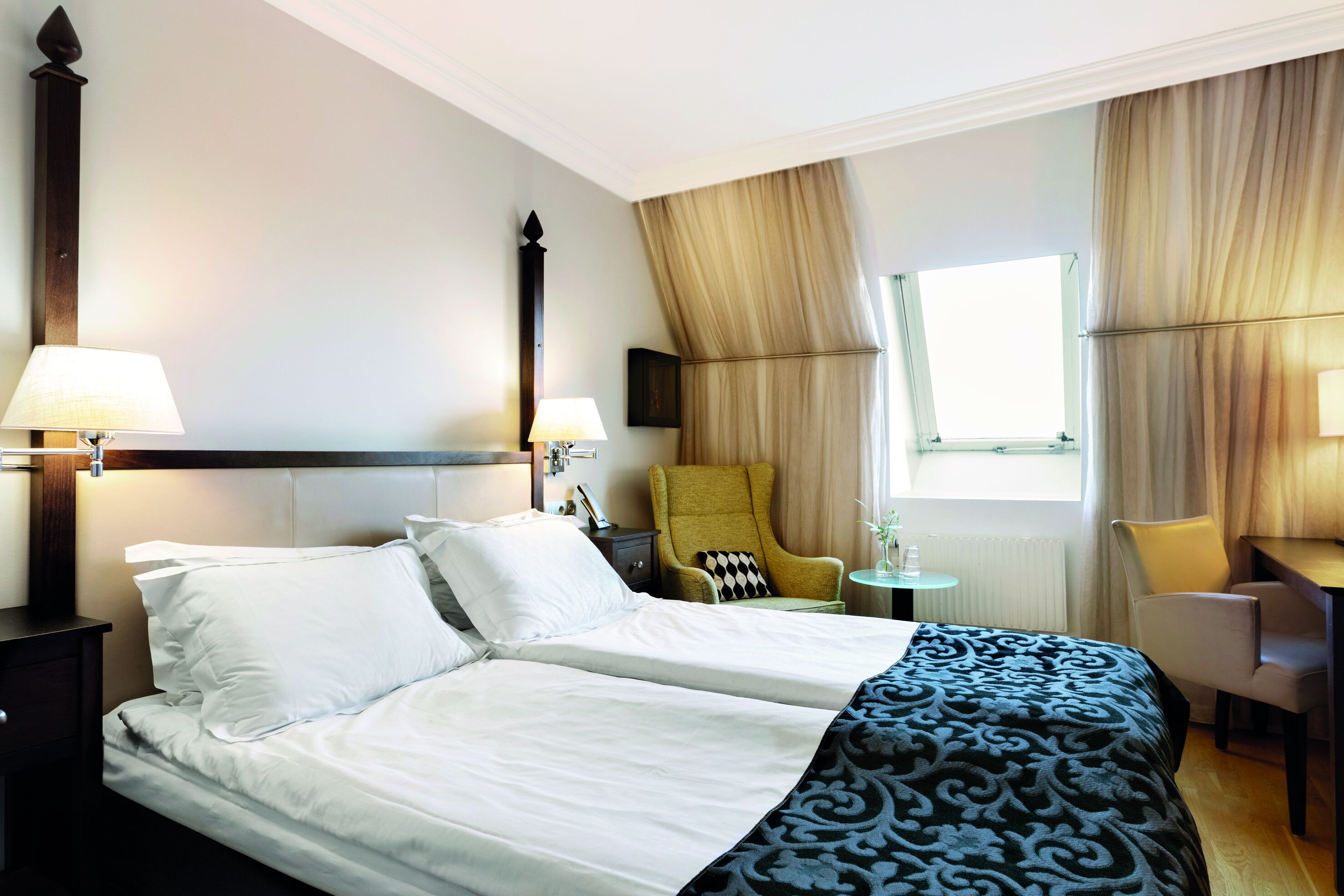 Habitación de hotel con cama, dos sillas, una mesita y una ventana con cortinas.