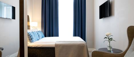 A hotel room with a bed, a chair, a TV, and a vase with flowers.