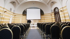 A conference room with rows of chairs, a large screen, and a high arched ceiling with intricate designs. - Elite Grand Hotel Norrköping (Norrköping)