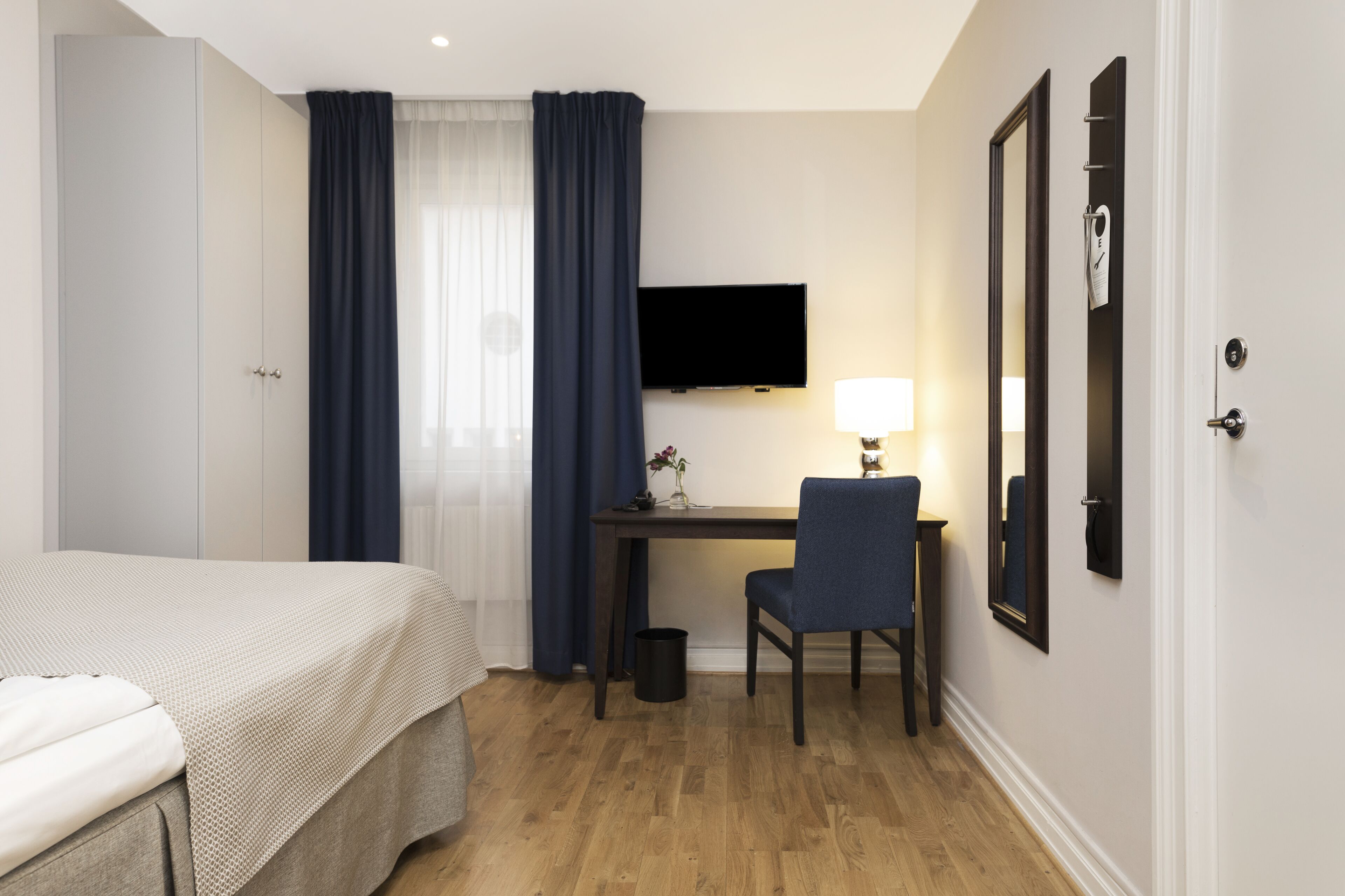 Habitación de hotel con cama, escritorio con silla, televisor y espejo montado en la pared.