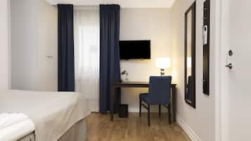 Habitación de hotel con cama, escritorio con silla, televisor y espejo montado en la pared.