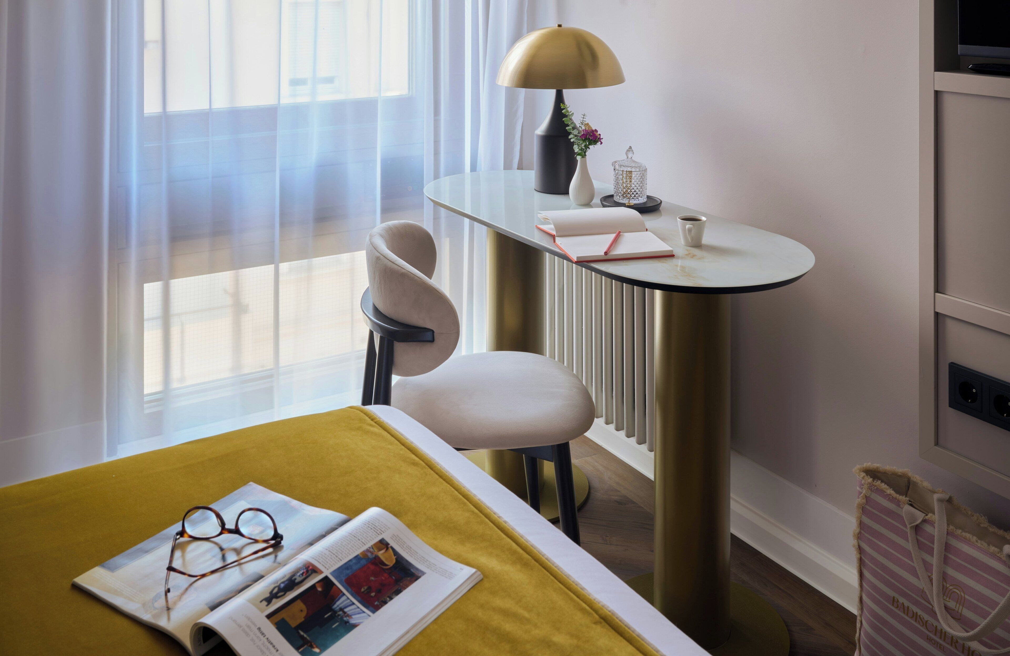 Ein Hotelzimmer mit Bett, Schreibtisch, Lampe, Stuhl und Heizkörper.