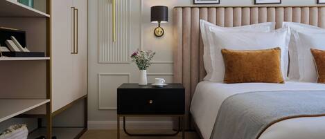 Une chambre d’hôtel avec un lit, une table de chevet avec une lampe, une étagère avec des livres et un tableau accroché au mur.