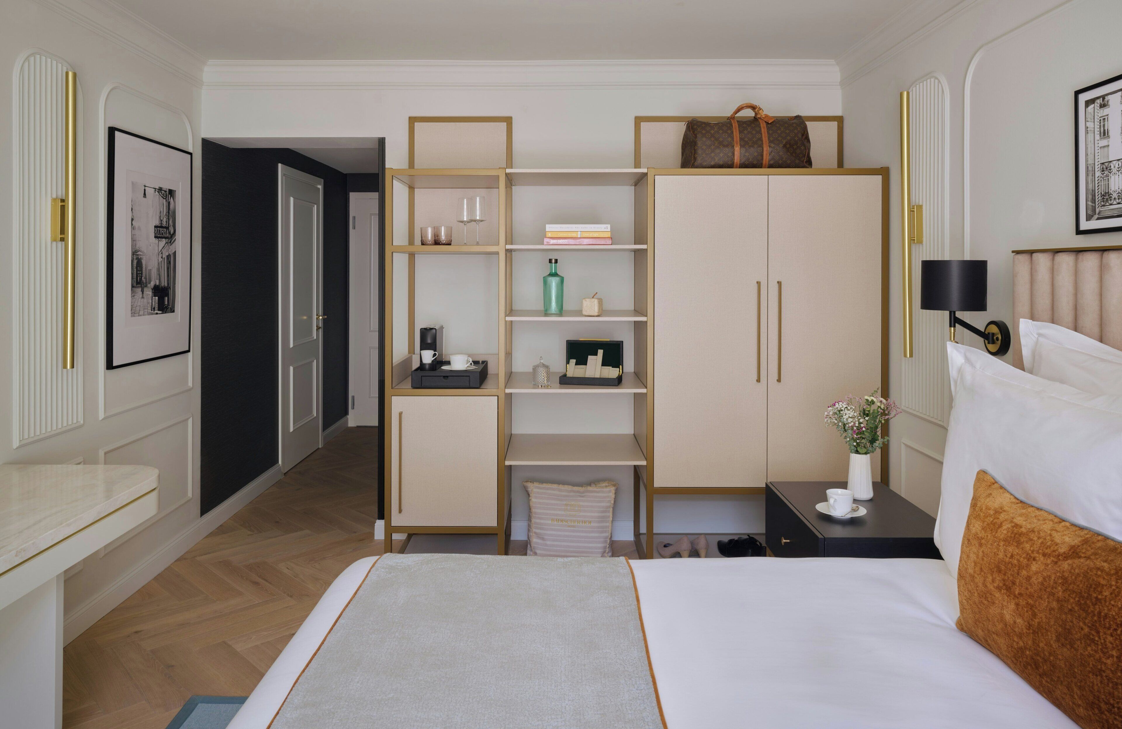 Hotelkamer met een bed, een kledingkast, een nachtkastje, een lijst met een foto en een deur naar een andere kamer.
