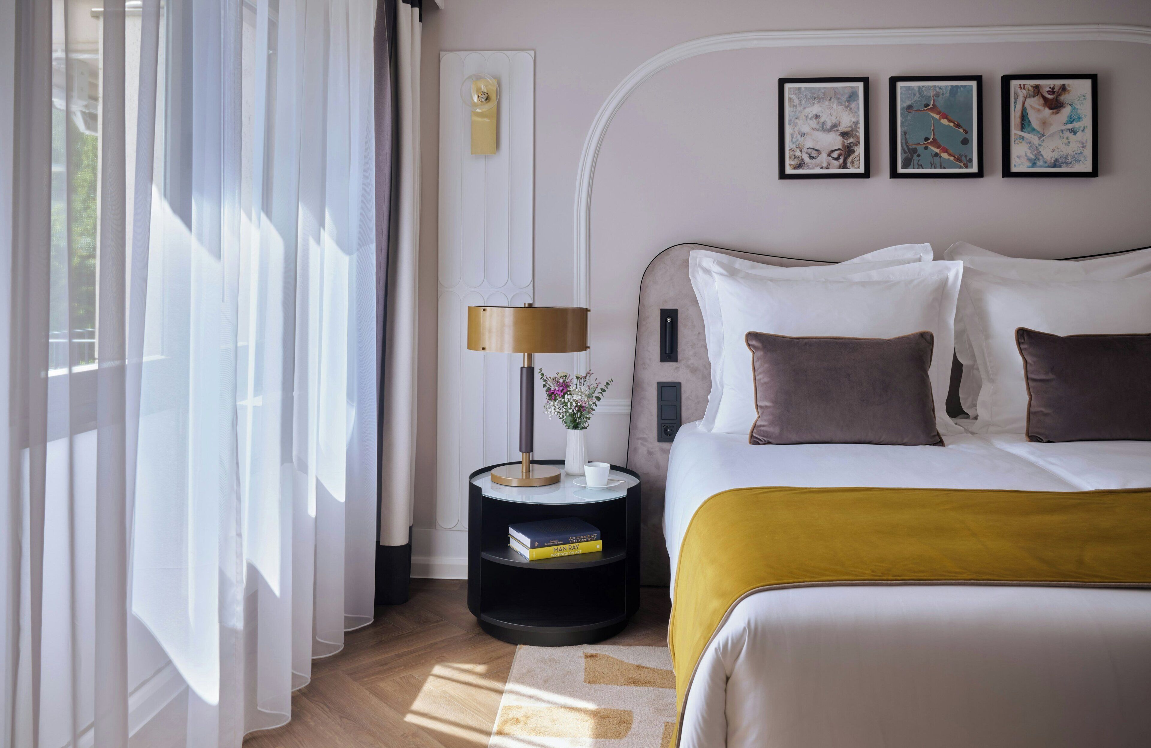 Ein Hotelzimmer mit Bett, Nachttisch mit Lampe, Blumenvase und Wandbildern.