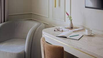A modern room with a white desk, a cushioned chair, a vase with flowers, a pair of glasses, a notebook, and a cup.