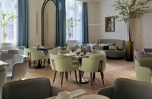 Uma sala de jantar moderna com mesas redondas, cadeiras estofadas em verde e um sofá.