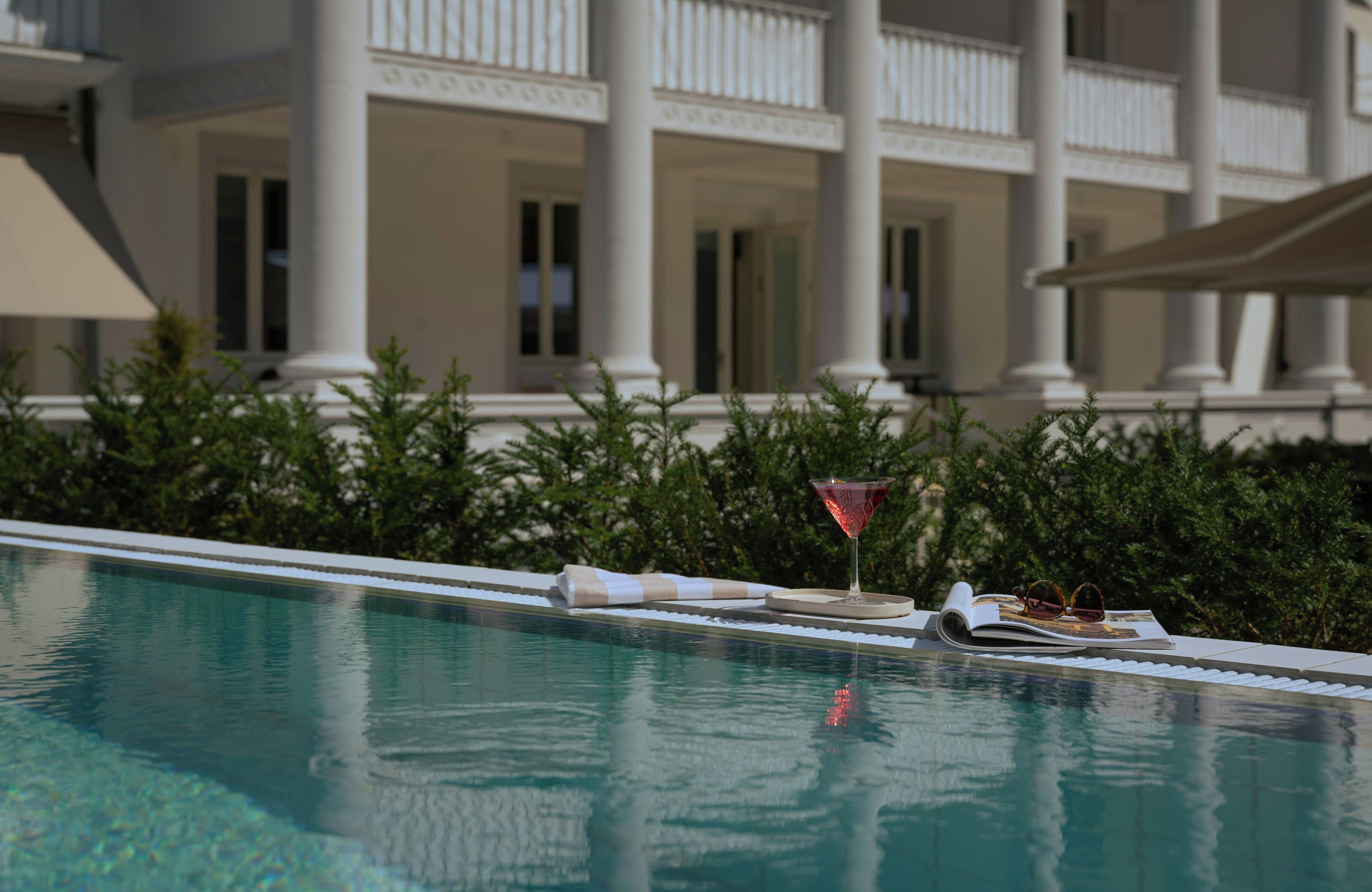 Piscina com área de descanso, um copo de martini e um livro.