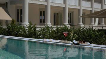 Piscina com área de descanso, um copo de martini e um livro.