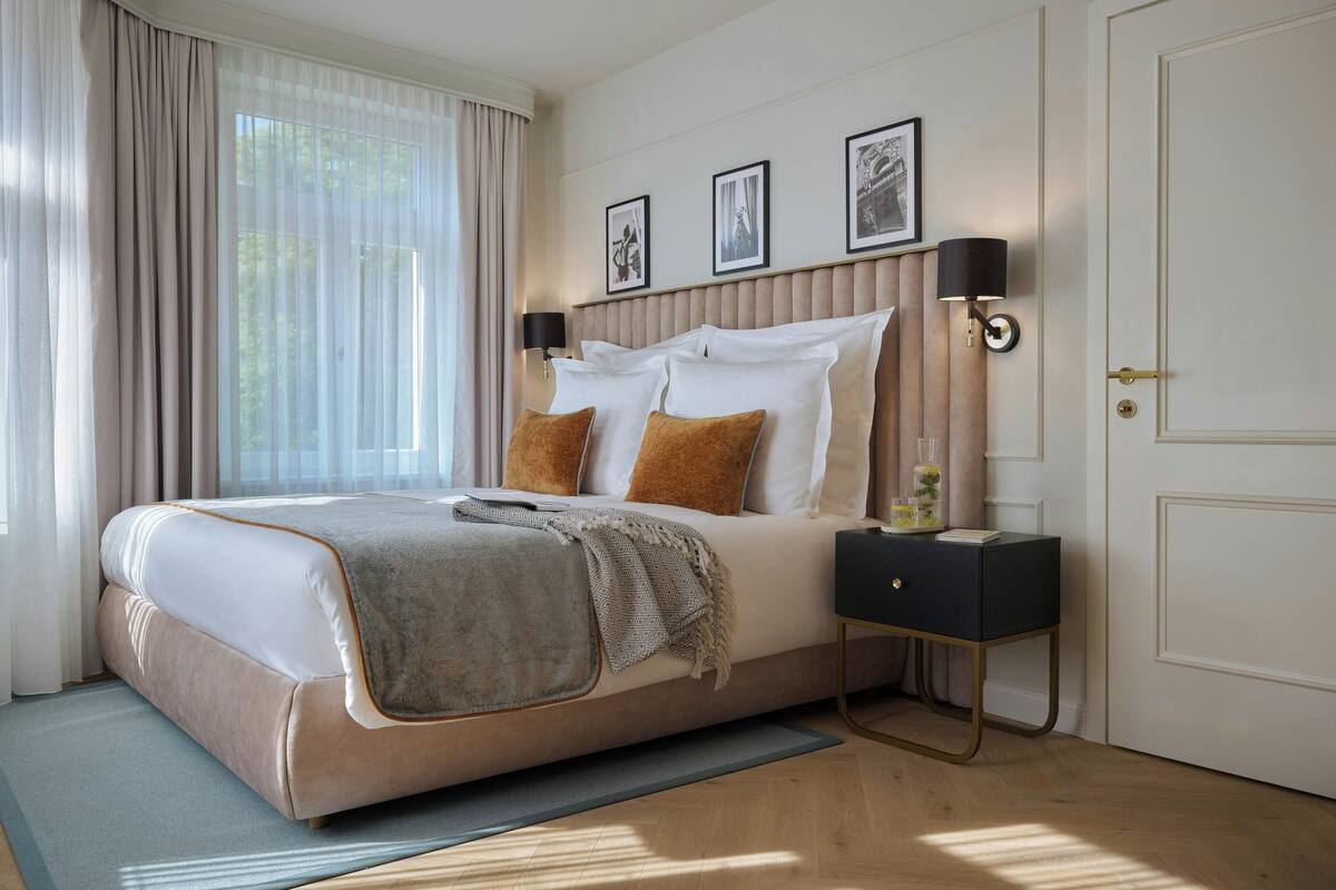 A modern hotel room with a large bed, a bedside table, a lamp, and framed pictures on the wall.