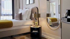Una habitación de hotel con cama, mesita de noche, lámpara, espejo y cafetera.
