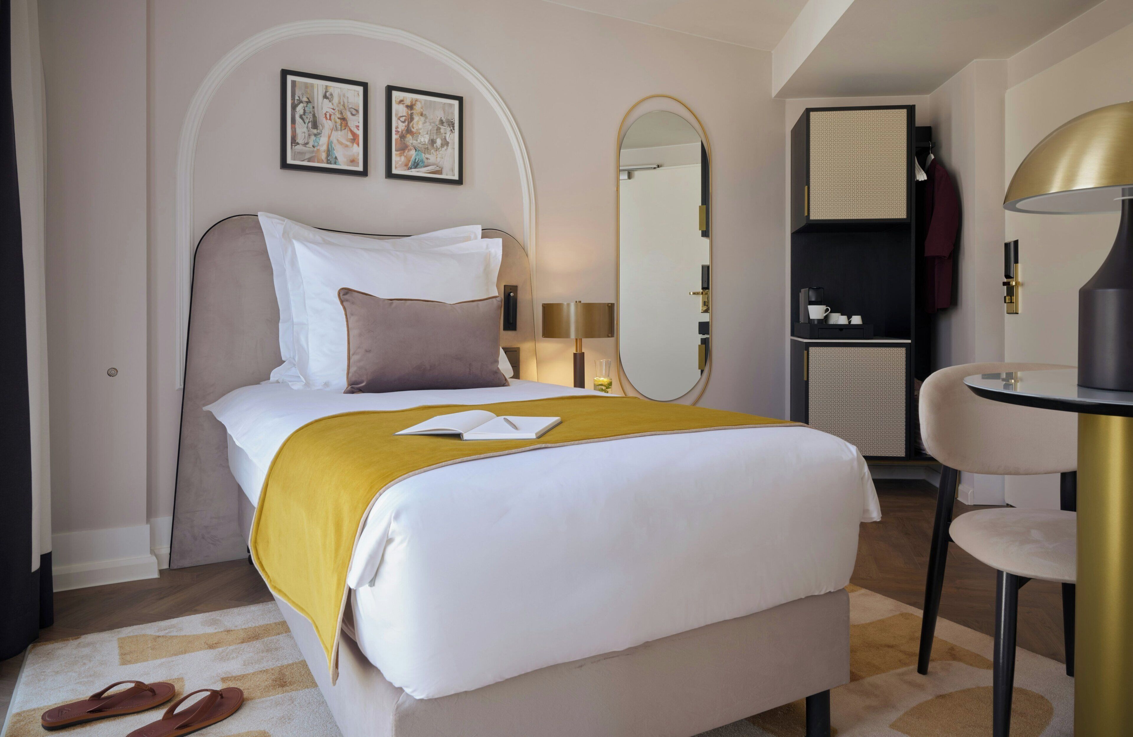 Une chambre d’hôtel avec un lit, un bureau, une chaise, un miroir et des œuvres d’art accrochées au mur.
