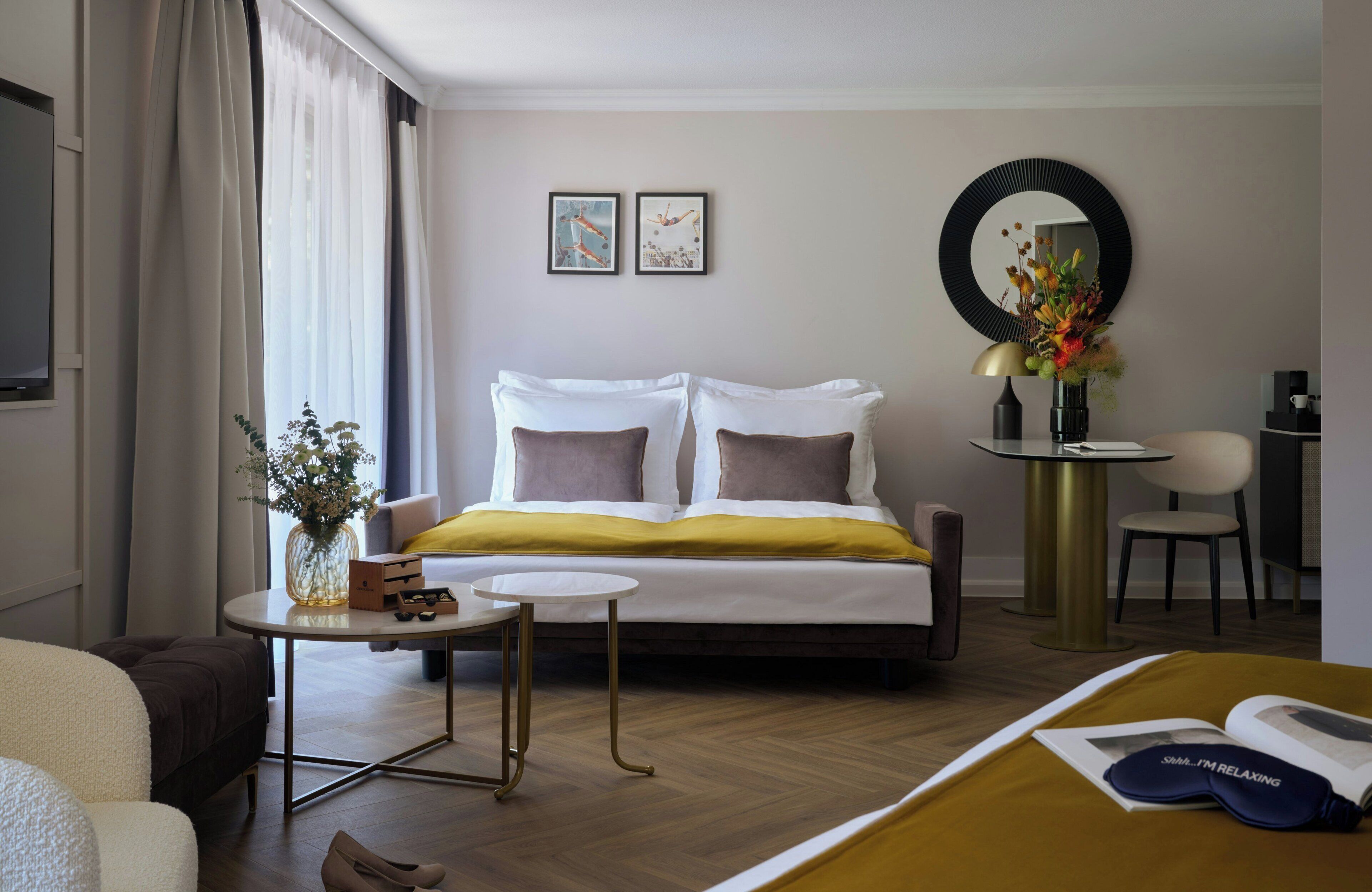Une chambre d’hôtel avec un lit, une petite table sur laquelle se trouve un vase, un miroir rond et une chaise.