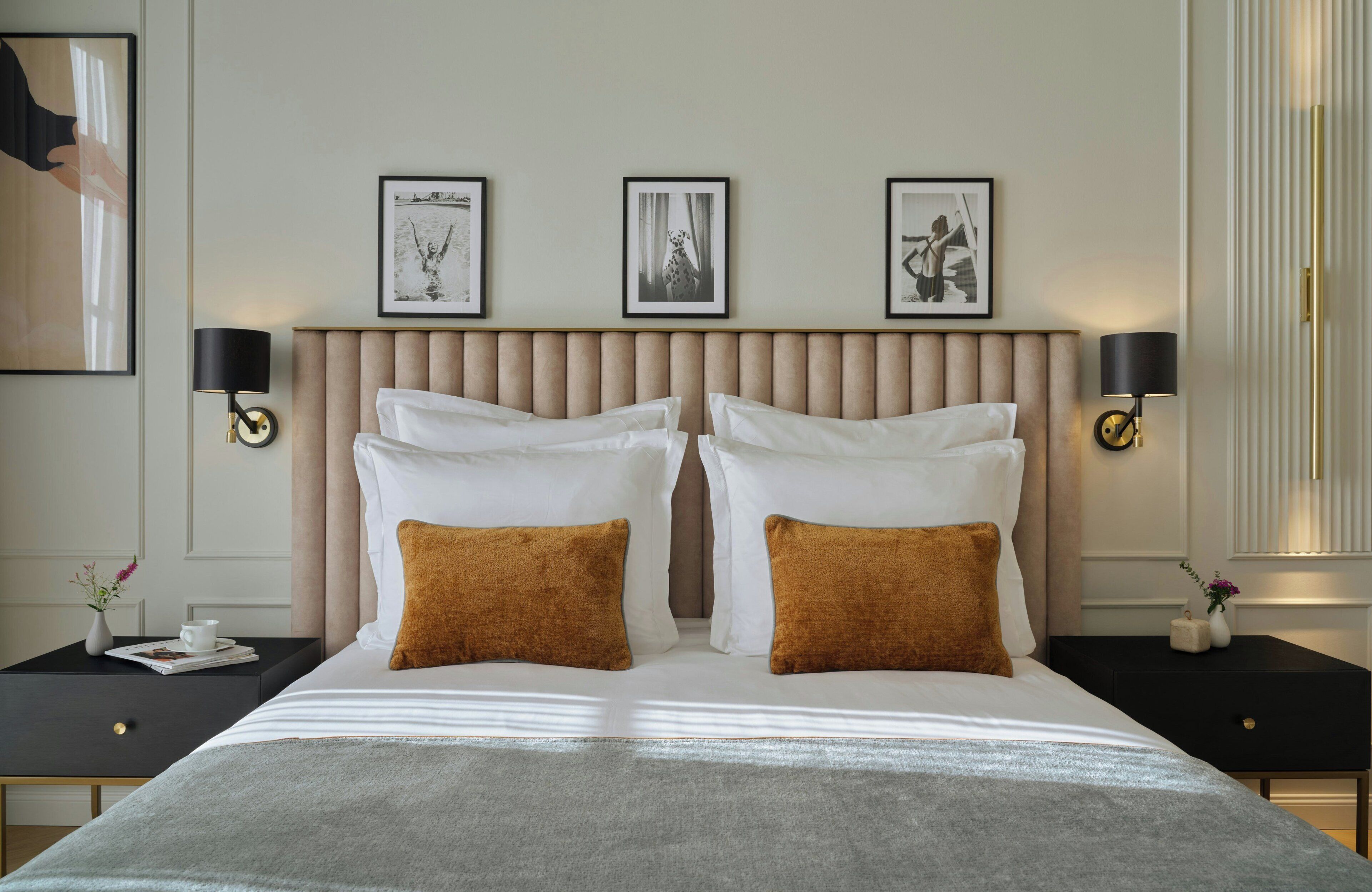A hotel room with a large bed, two bedside tables, a headboard with three framed pictures, and two wall-mounted lamps.