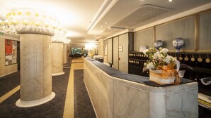 Zona de recepción de hotel con columnas de mármol, un mostrador de recepción y un sistema de tarjetas de acceso en la pared.