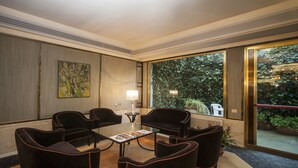 Una habitación de hotel moderna con un ventanal grande, una mesa de centro de vidrio y varias sillas tapizadas.