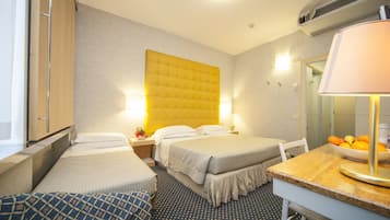 Ein Hotelzimmer mit zwei Betten, einem kleinen Tisch mit einer Obstschale, einer Lampe und einem Spiegel.