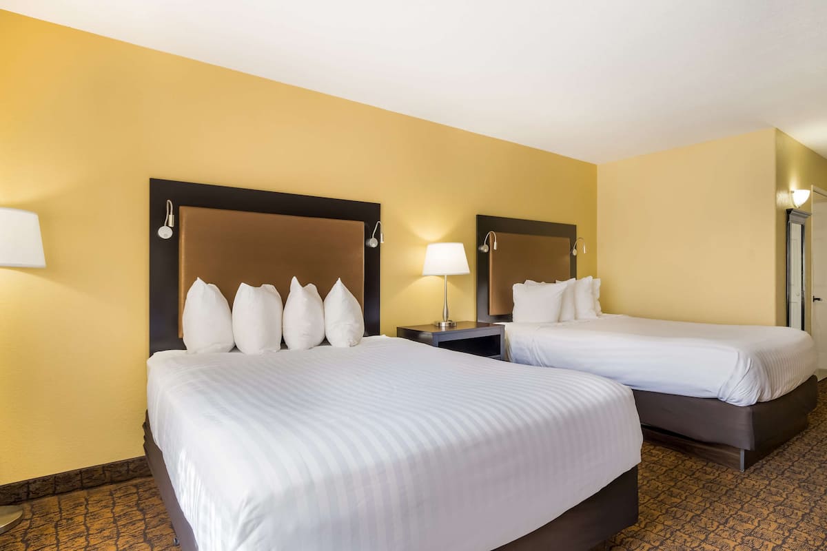 A hotel room with two beds, each with a headboard and bedside lamps.