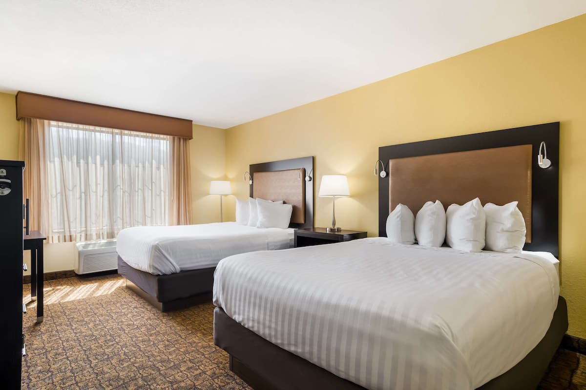 A hotel room with two beds, a desk, and a window with curtains.