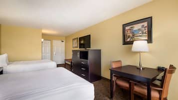 A hotel room with two beds, a desk with a chair, a TV, a lamp, and a painting on the wall.