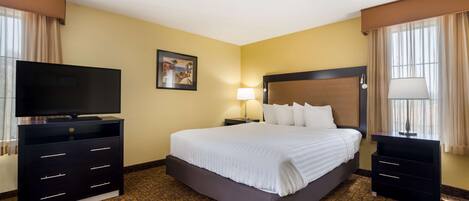 A hotel room with a large bed, a TV on a dresser, a nightstand with a lamp, and a painting on the wall.