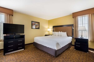 A hotel room with a large bed, a TV on a dresser, a nightstand with a lamp, and a painting on the wall.