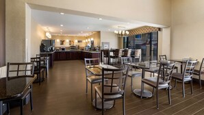 A spacious hotel dining area with multiple tables and chairs, a central kitchen area, and a view of the cityscape through large windows. - Best Western Escondido Hotel (Escondido)