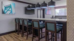Un bar d’hôtel doté d’un long comptoir, de nombreux tabourets et d’un éclairage suspendu.