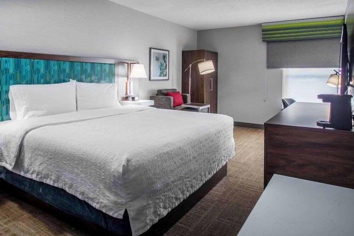 A hotel room with a large bed, a desk, a chair, a wardrobe, and a window with a view.