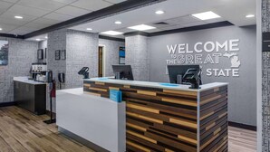 Un comptoir d’accueil moderne, agrémenté d’une pancarte « Bienvenue dans le magnifique État », d’un écran numérique et d’un présentoir portant l’inscription « Hilton ».