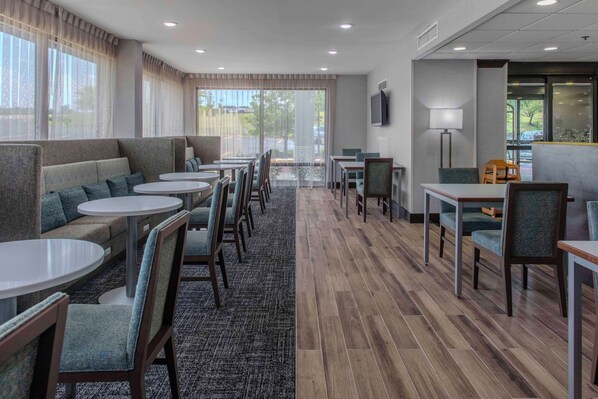 Un hall d’hôtel doté d’espaces aménagés avec des sièges, des tables et une grande fenêtre offrant une vue panoramique.