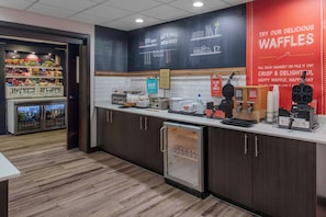 A bakery counter with waffle-making equipment, a refrigerated display case, and a sign advertising waffles.