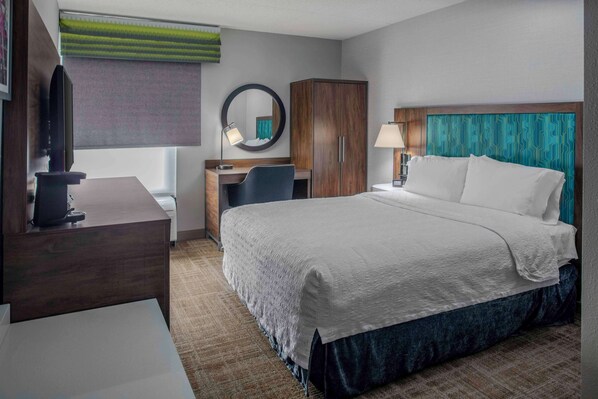 A hotel room with a bed, a desk, a chair, a television, a wardrobe, and a mirror.