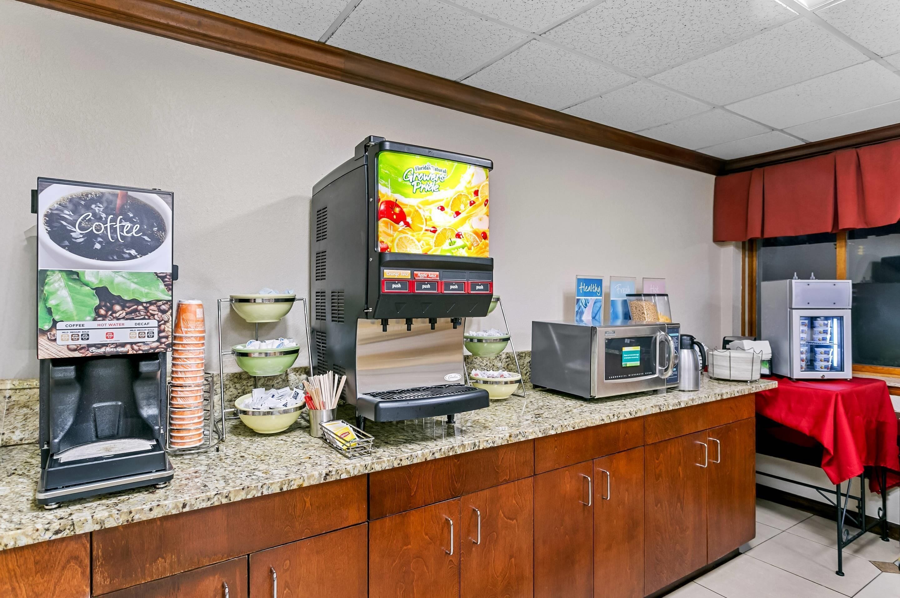 En kaffestation med en kaffemaskin, en juiceautomat och en mikrovågsugn, placerad på en bänkskiva av granit.