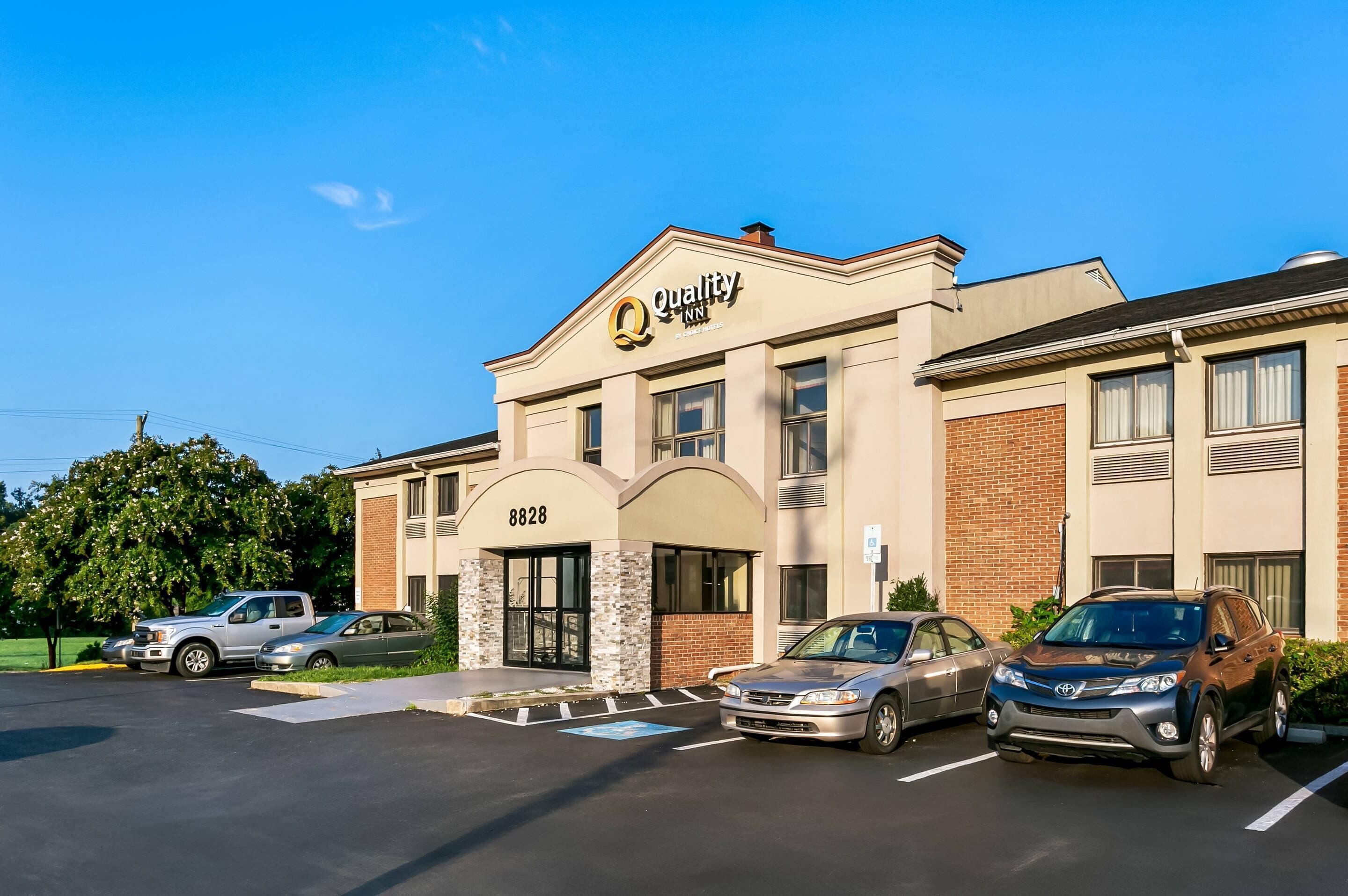 A hotel with a prominent sign, a brick facade, and a parking lot with several cars.