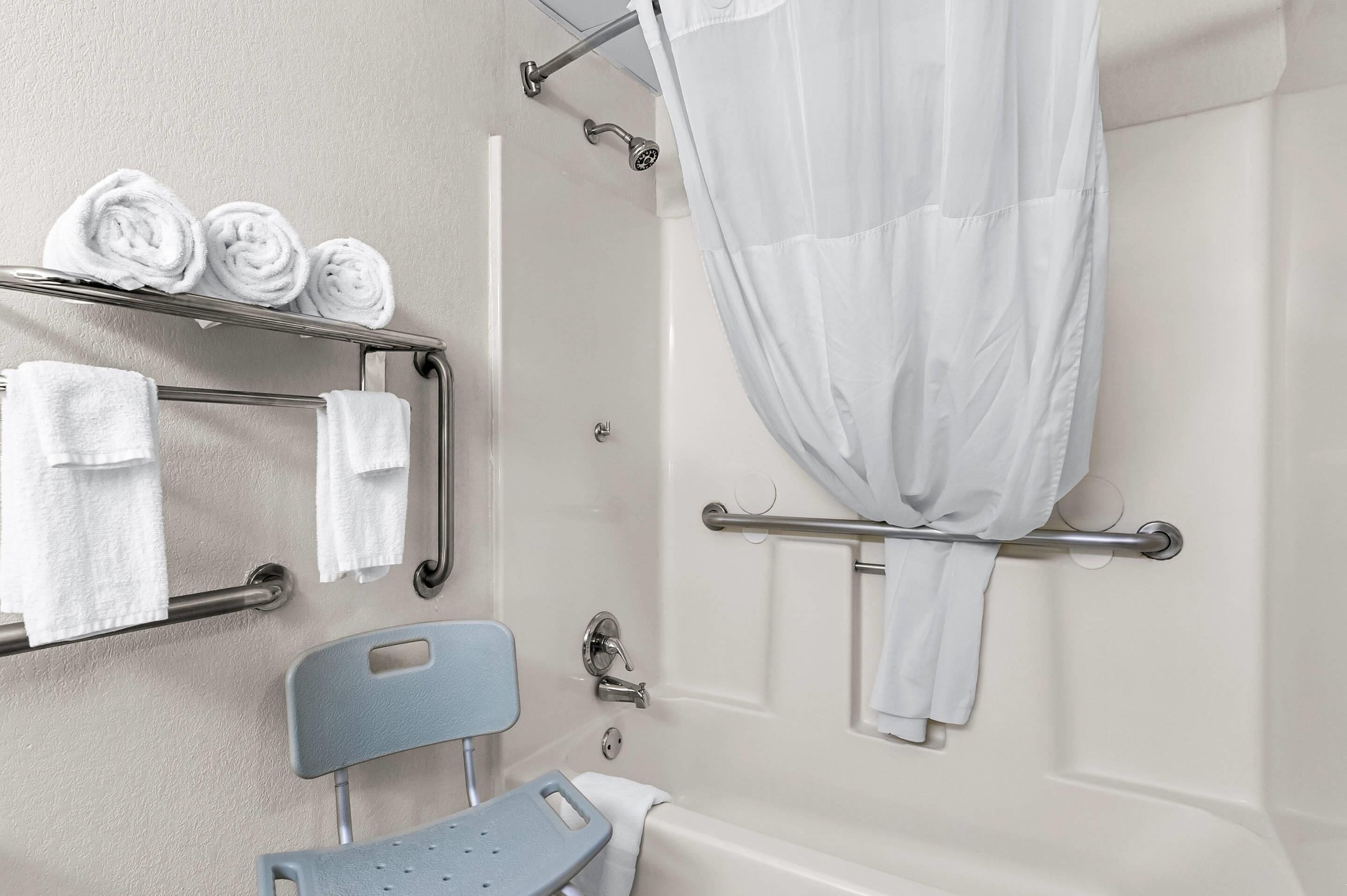 Une salle de bain équipée d’un rideau de douche, d’un porte-serviettes avec des serviettes, d’une barre d’appui et d’un siège de douche.