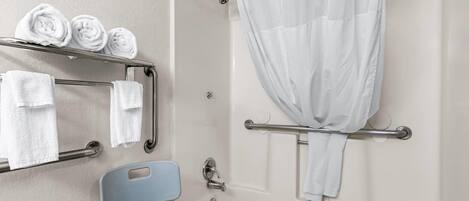 Une salle de bain équipée d’un rideau de douche, d’un porte-serviettes avec des serviettes, d’une barre d’appui et d’un siège de douche.