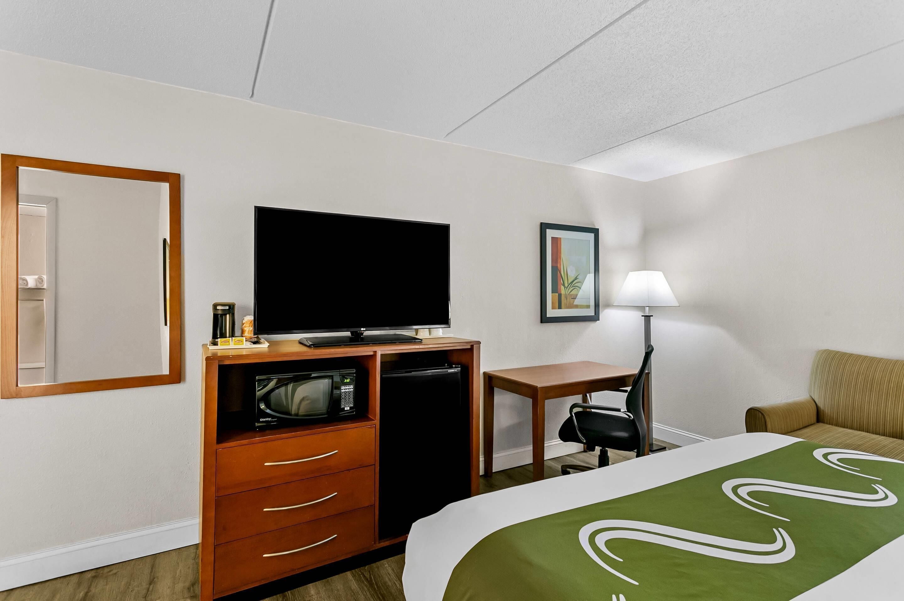 Une chambre d’hôtel équipée d’un lit, d’une télévision, d’un four à micro-ondes, d’un réfrigérateur, d’un bureau, d’une chaise, d’une lampe et d’un tableau encadré au mur.