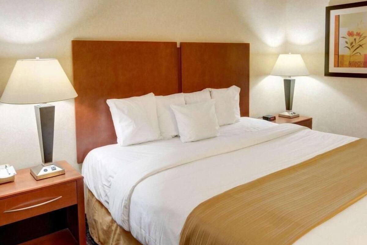 Hotellihuone, jossa on sänky, kaksi yöpöytää, lamput ja seinällä oleva kehystetty kuva.