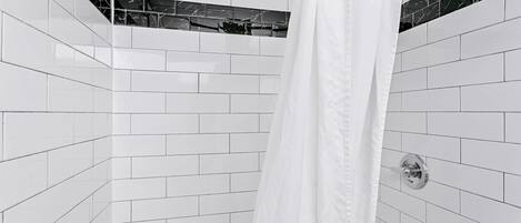 A bathroom with white tiled walls, a shower curtain, and a chrome faucet.