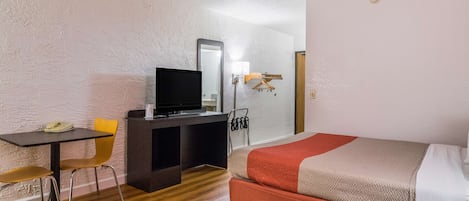 Una habitación de hotel con cama, escritorio con televisor, silla y armario.
