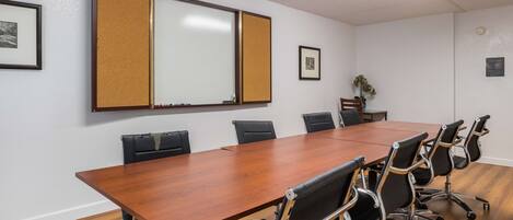 A conference room with a long wooden table, black office chairs, a whiteboard, and framed pictures on the walls.