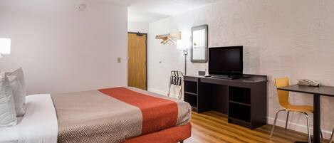 Habitación de hotel con una cama, un escritorio con computadora, una silla y un televisor.