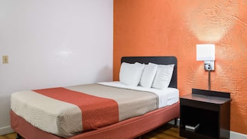 Una cama individual con una colcha roja y blanca, una almohada blanca y una mesita de noche con una lámpara.