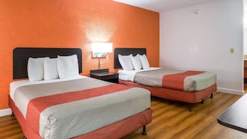 Two beds with red and grey bedding, a nightstand with a lamp, and a wooden floor.