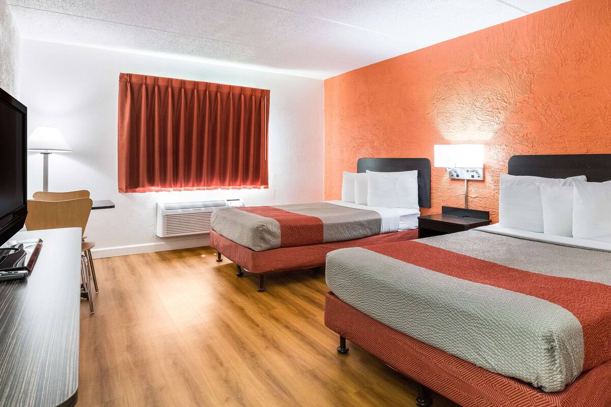 A hotel room with two beds, a desk, a chair, a TV, and a window with curtains.