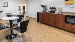 A clean, modern cafe with a coffee machine, a menu board, and a seating area with tables and chairs.