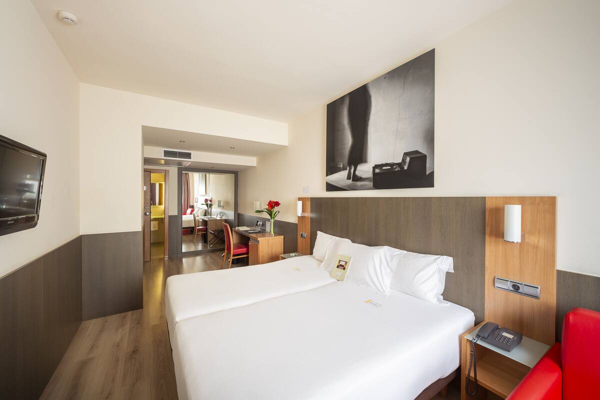 A hotel room with a large bed, a desk, a chair, a TV, and a painting on the wall.